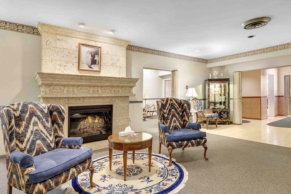 Cozy living room with stone fireplace, patterned chairs, round table, and beige carpet