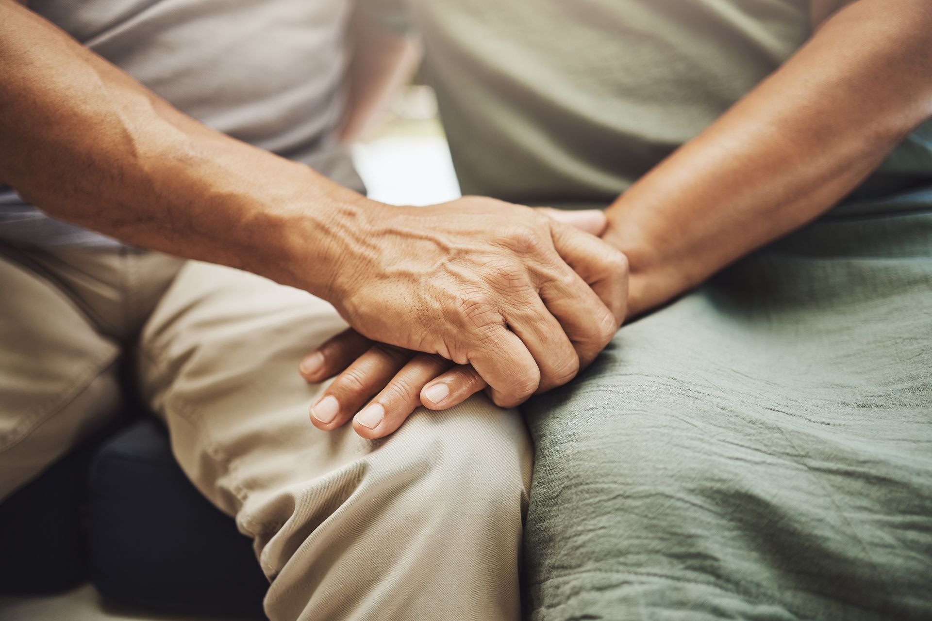 Two hands clasped together on a lap, suggesting comfort and support