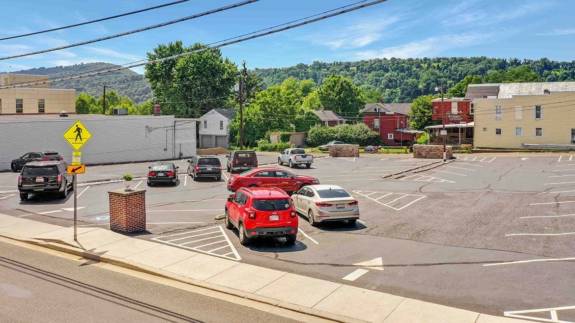 Parking lot with several cars, including a red sports car in front, beside low buildings under a blue sky.