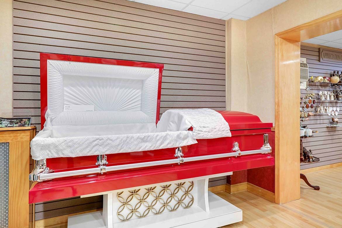 Red casket displayed in a funeral showroom with white lining and a beige-striped wall.