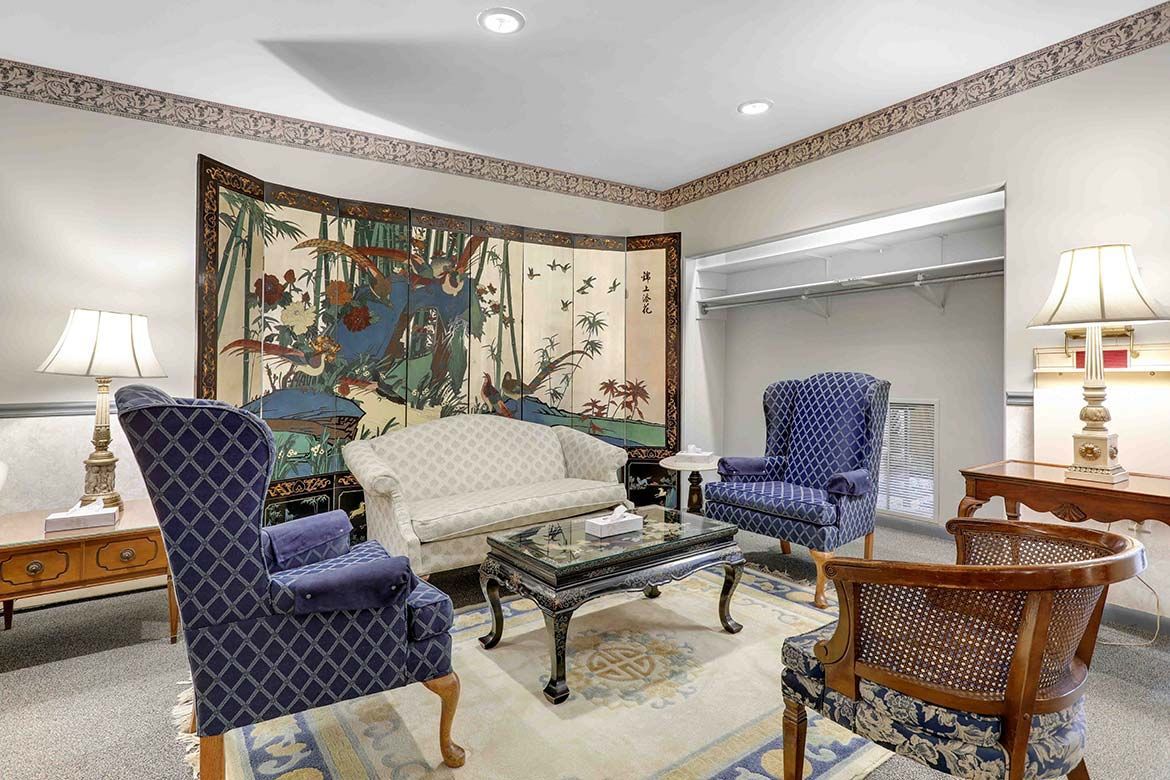 Elegant living room with blue upholstered chairs, cream sofa, glass coffee table, and colorful wall tapestry