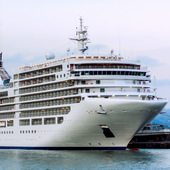Large white cruise ship docked at a port, viewed from the front side