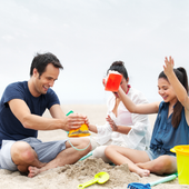 Friends on a beach picnic, sharing drinks and smiling in the sand.