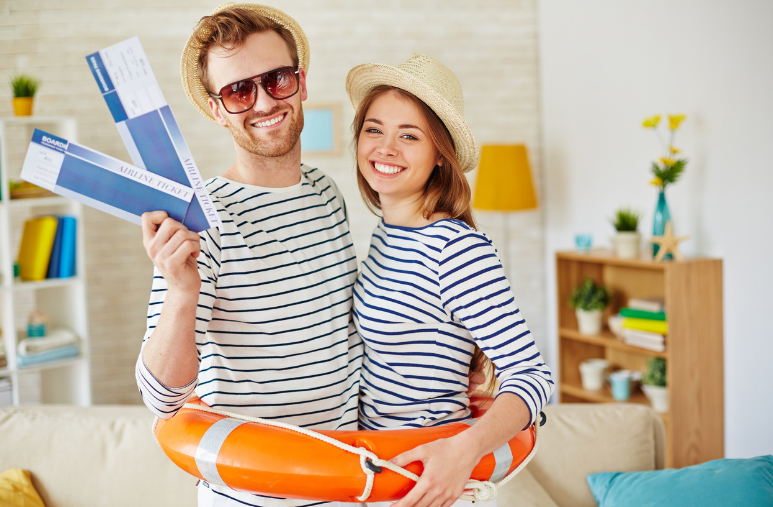 Smiling couple holding a life ring and travel brochures in a bright living room