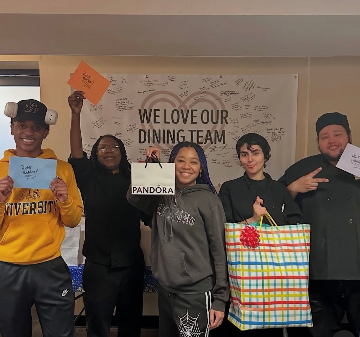 Group of dining staff holding gifts and signs in front of a banner that says