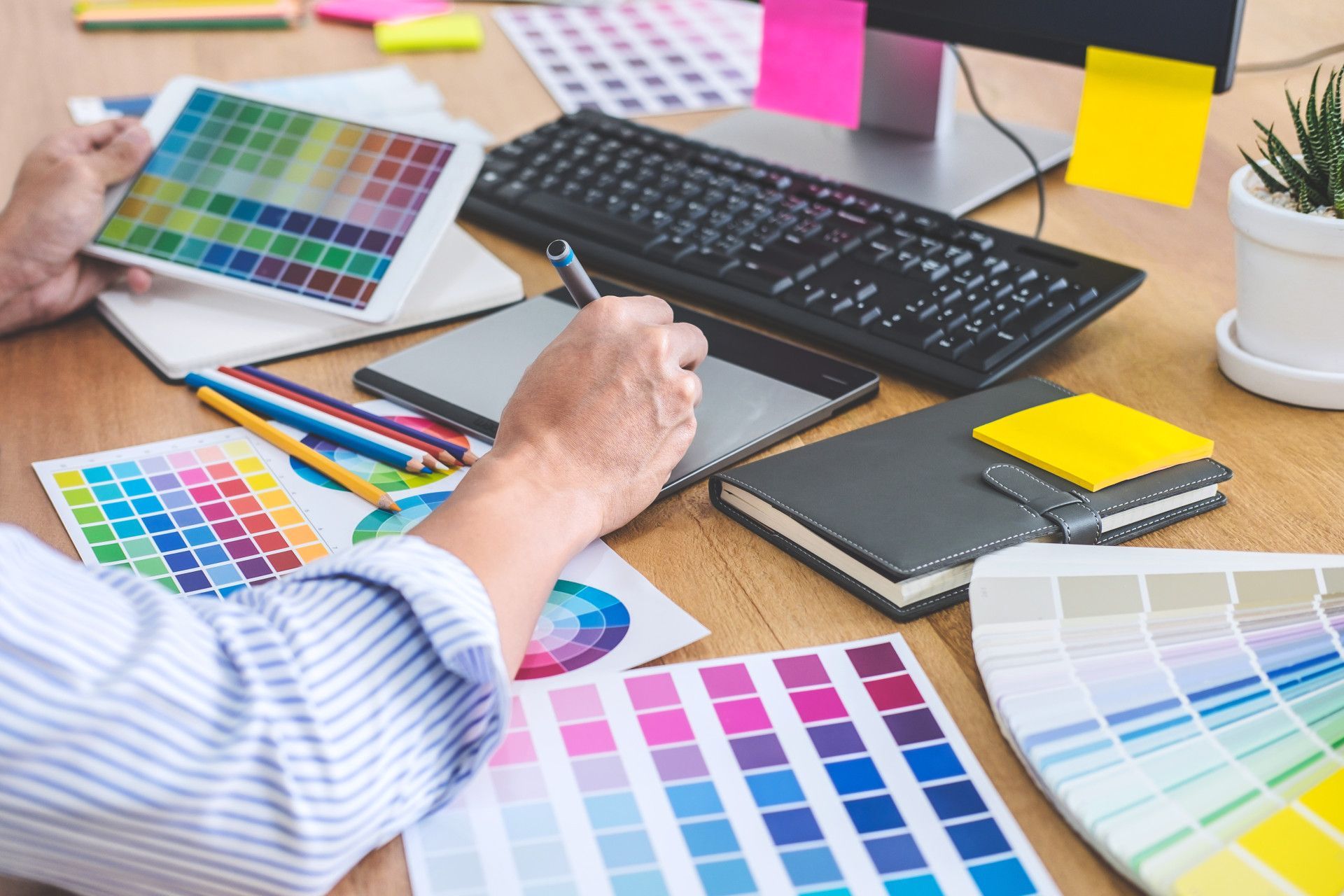 A designer working at a desk with color swatches, a digital tablet, stylus, and a computer screen.