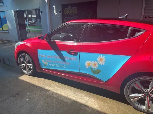 A bright red car parked outside, featuring a large blue advertisement decal on the door decorated with daisy graphics.