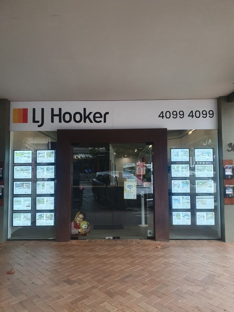 The storefront of an LJ Hooker real estate office featuring lit window displays of property listings.