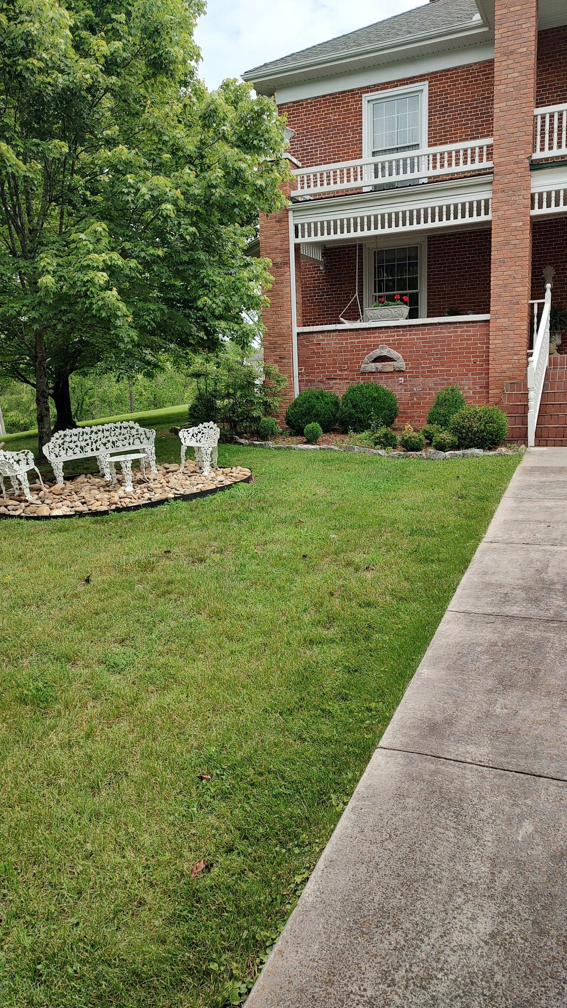 Brick apartment building with white balcony, green lawn, white chairs, and a concrete sidewalk in front