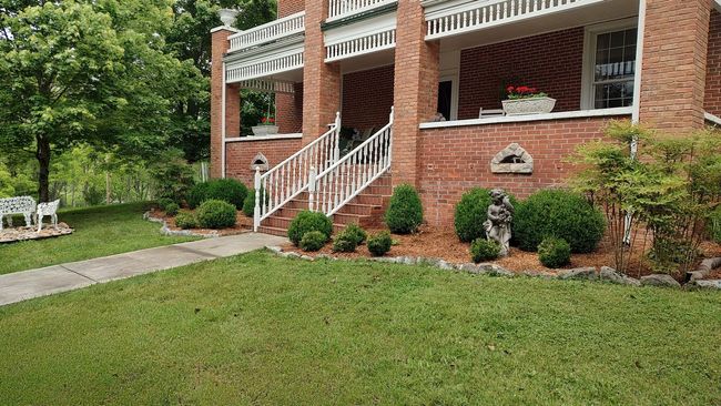 Brick house porch with white railing, steps, shrubs, and a green front lawn