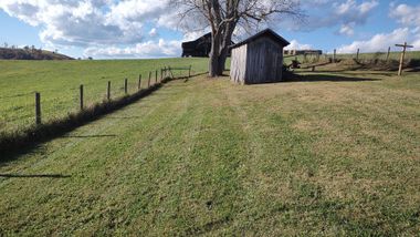 Rural path through a grassy field beside a small wooden shed and fence under a blue sky