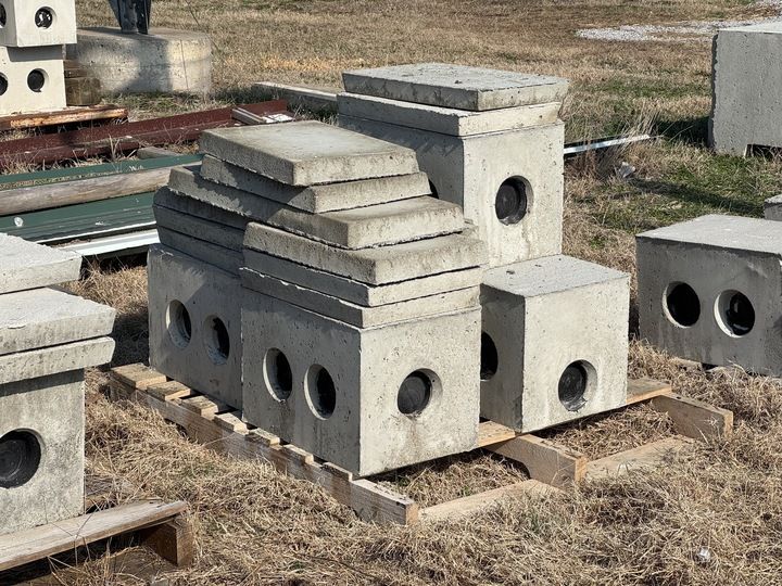 Concrete drainage boxes and covers stacked on a pallet outdoors, with circular openings.