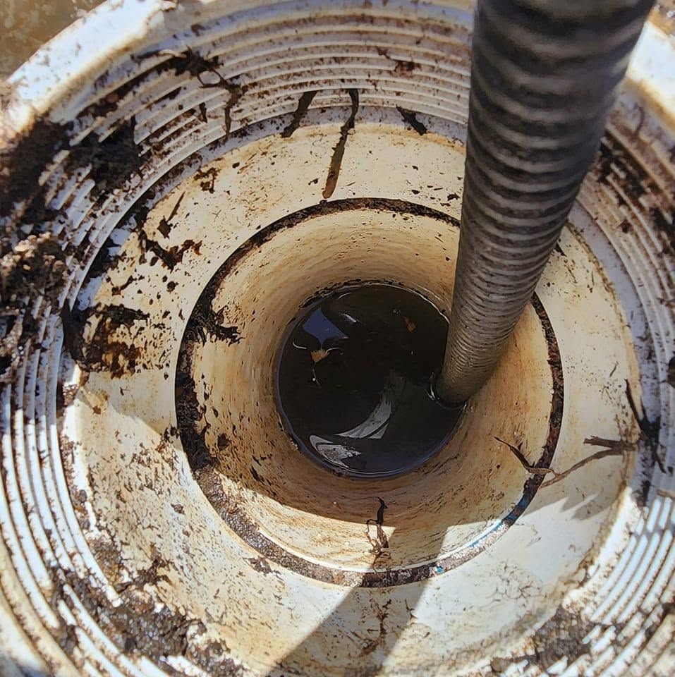 Looking down into a dirty white pipe or tank with a flexible hose lowered inside.
