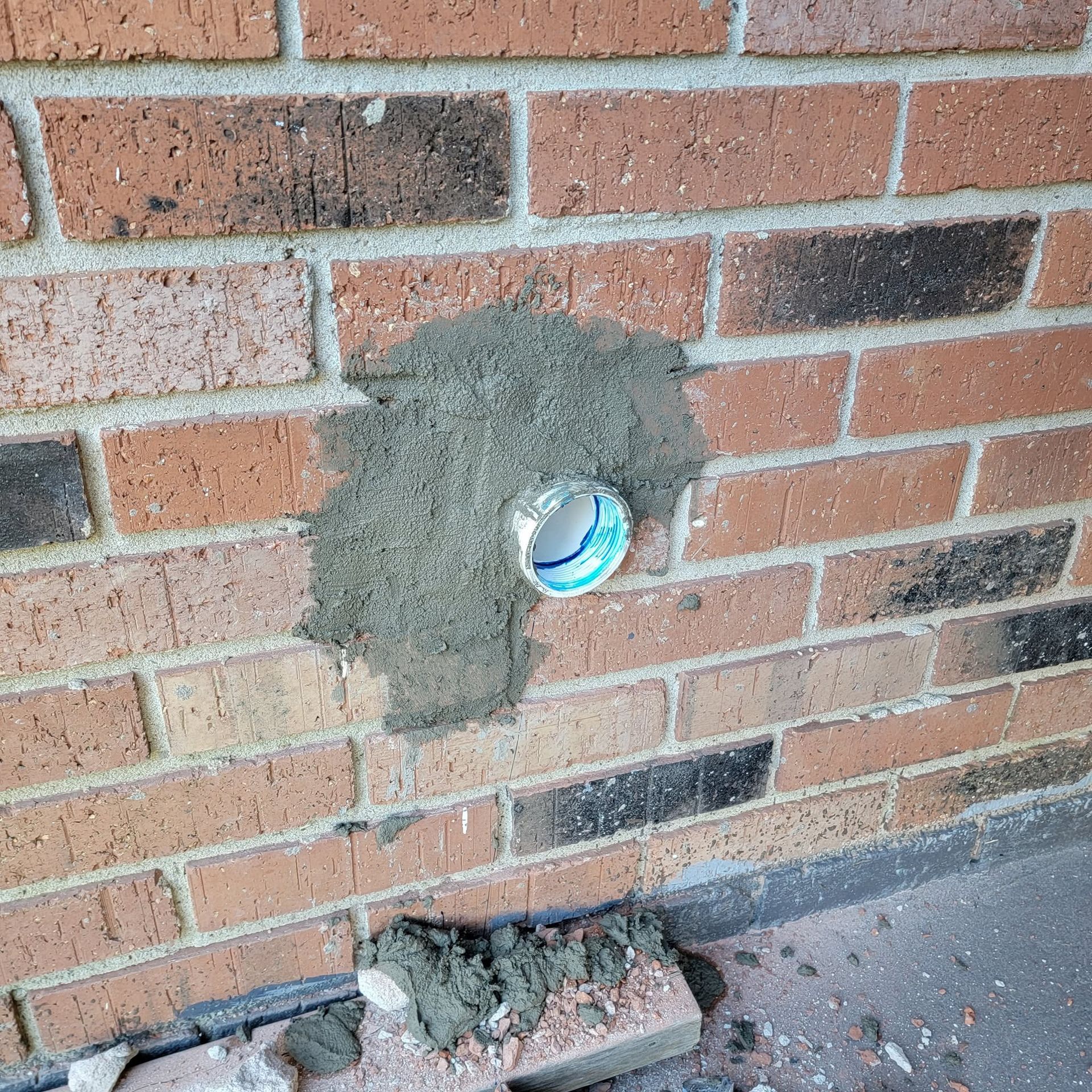 Brick wall with a patched circular hole exposing a blue pipe opening near the bottom.
