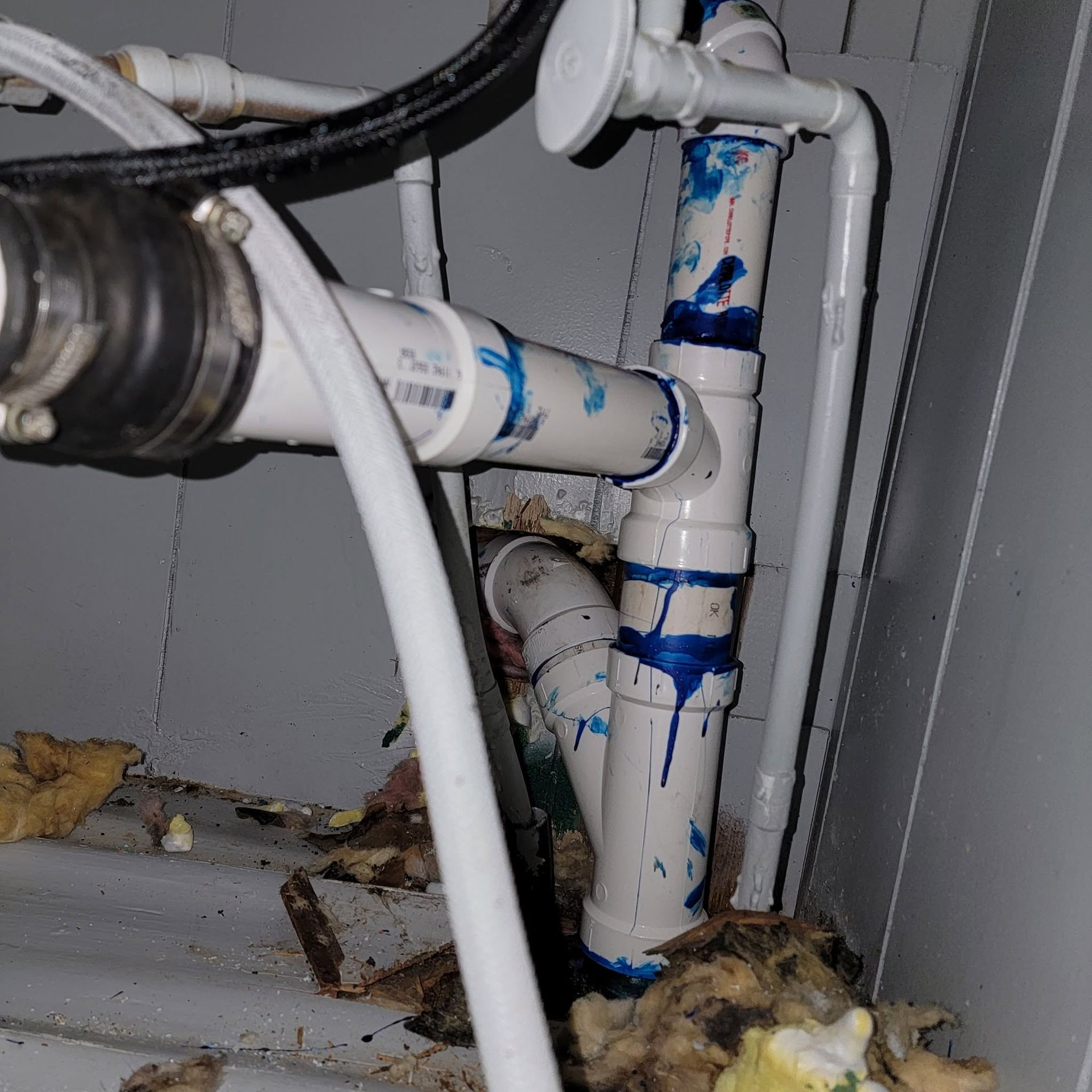 Under-sink plumbing with white PVC pipes and blue tape, showing leaks or residue inside a cabinet.