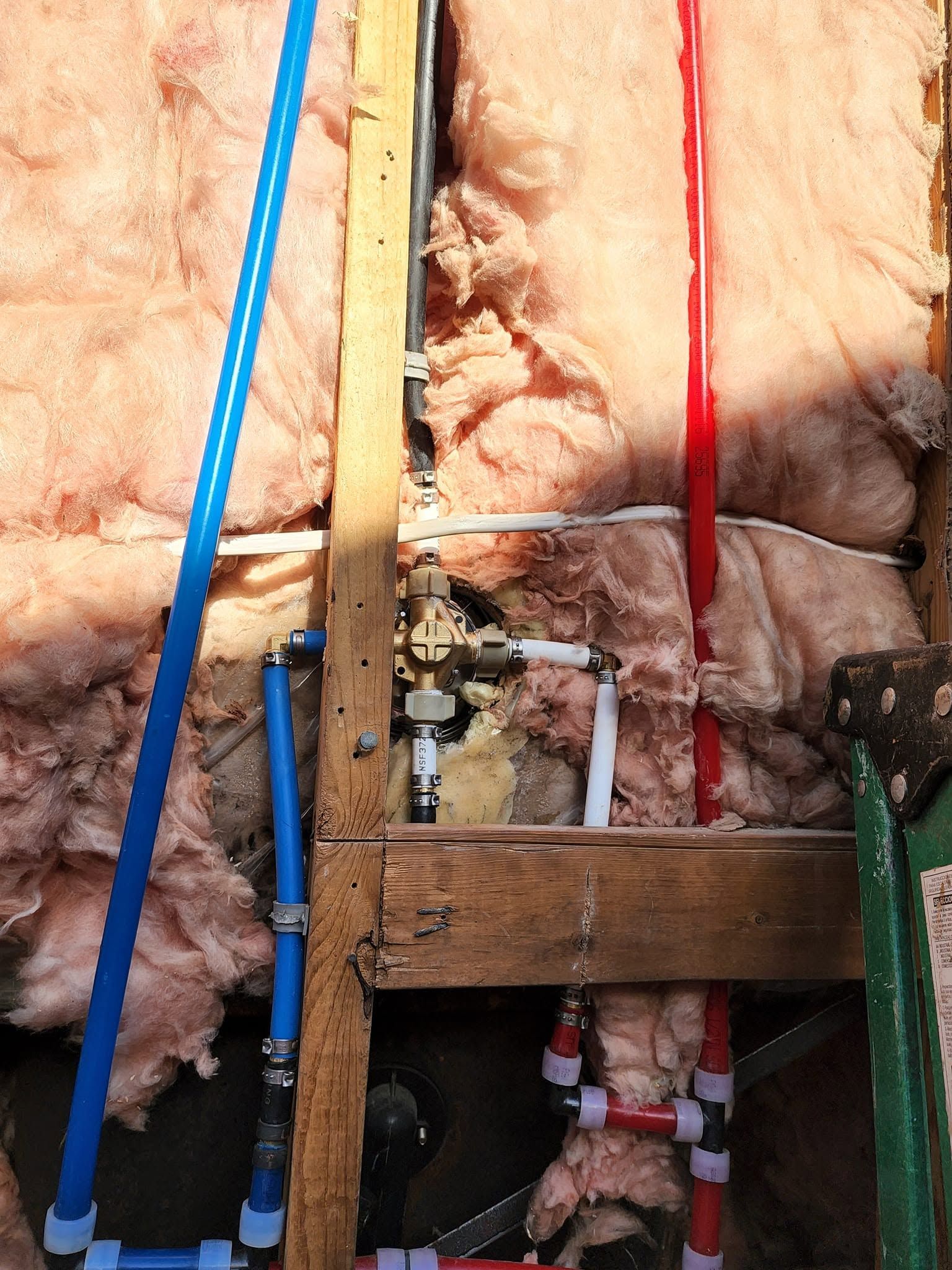 Exposed plumbing and insulation inside a wall with blue and red pipes and a wooden support frame