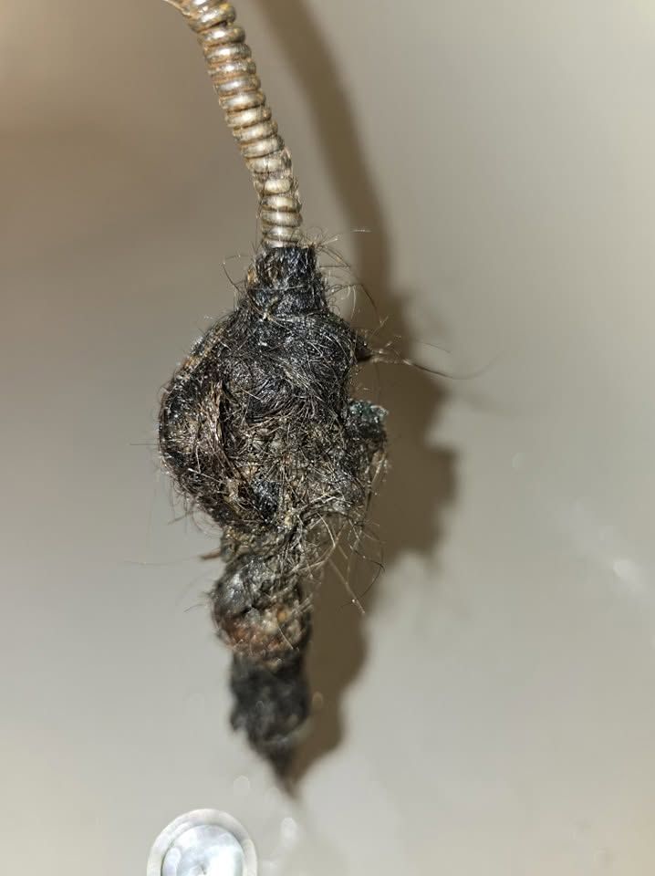 Close-up of a tangled dark clump hanging from a flexible metal hose against a beige surface