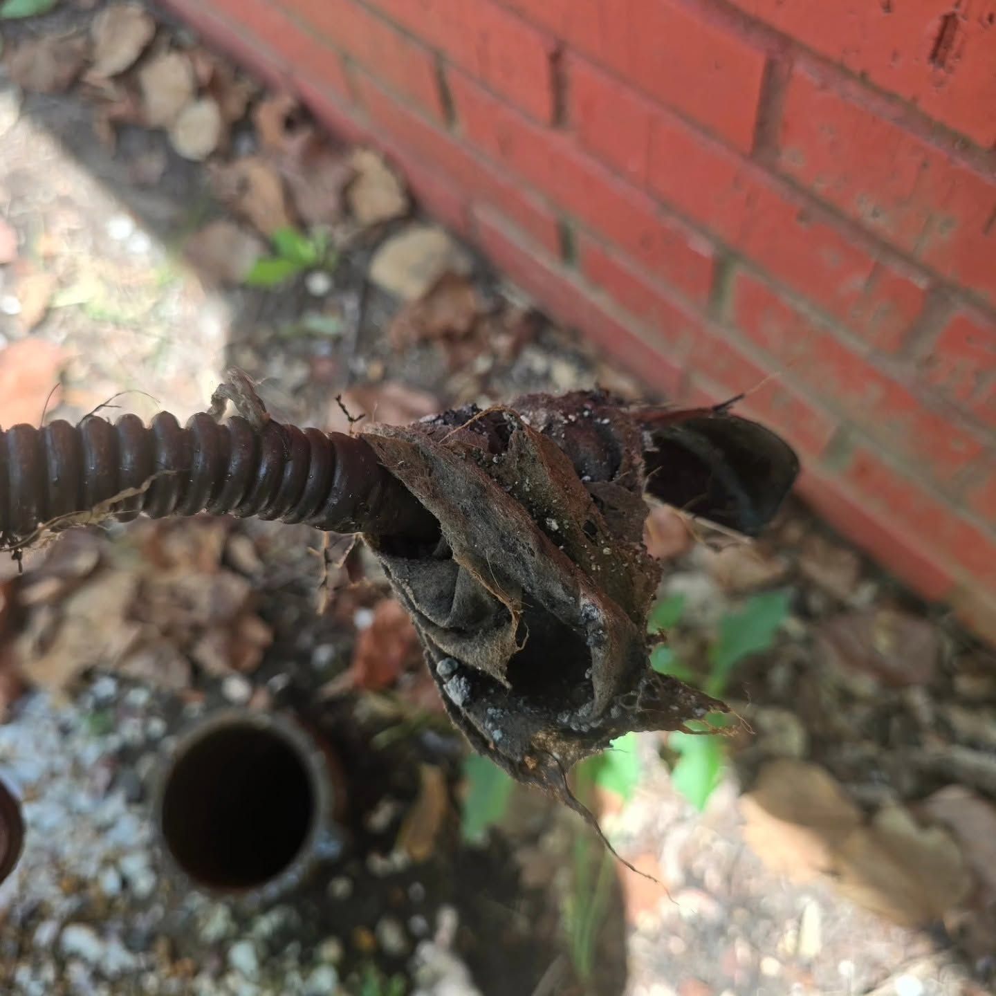 Rusty metal rod with a corroded clamp near a brick wall and ground debris
