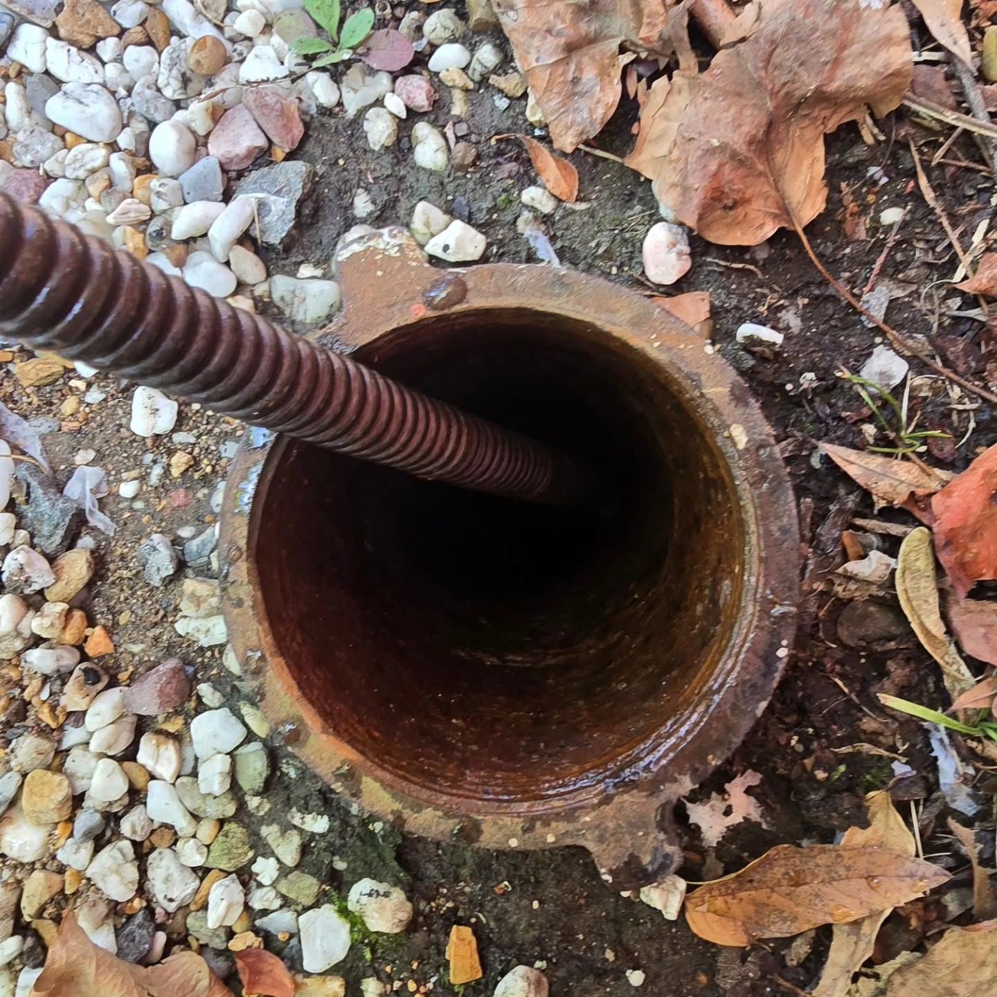 Open rusty pipe in gravel with a metal rod inserted inside