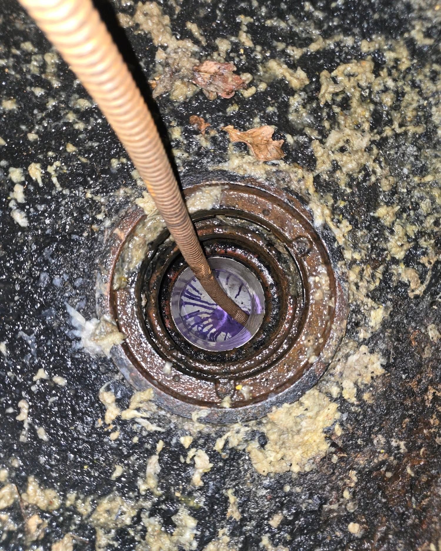 Close-up of a rusty drain opening with a hose inserted into dark, dirty water.