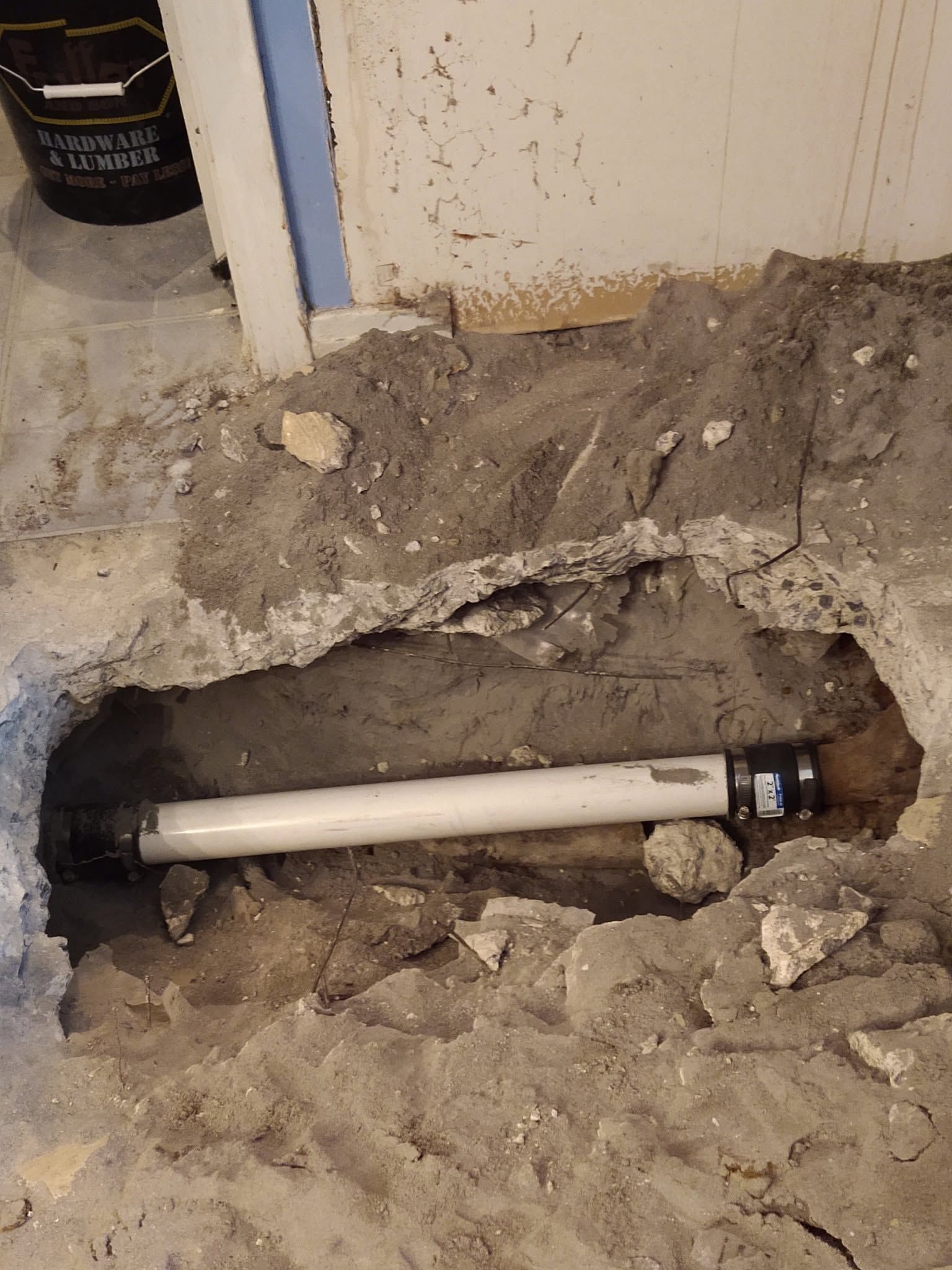 Broken concrete floor exposing a white pipe in a rough hole near a wall and doorway.