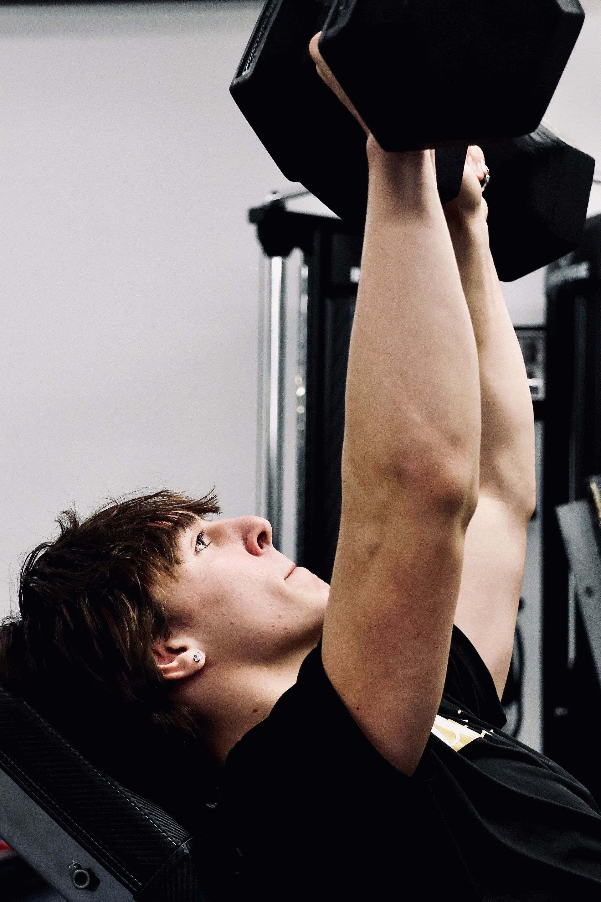 A man is lifting a dumbbell over his head in a gym.