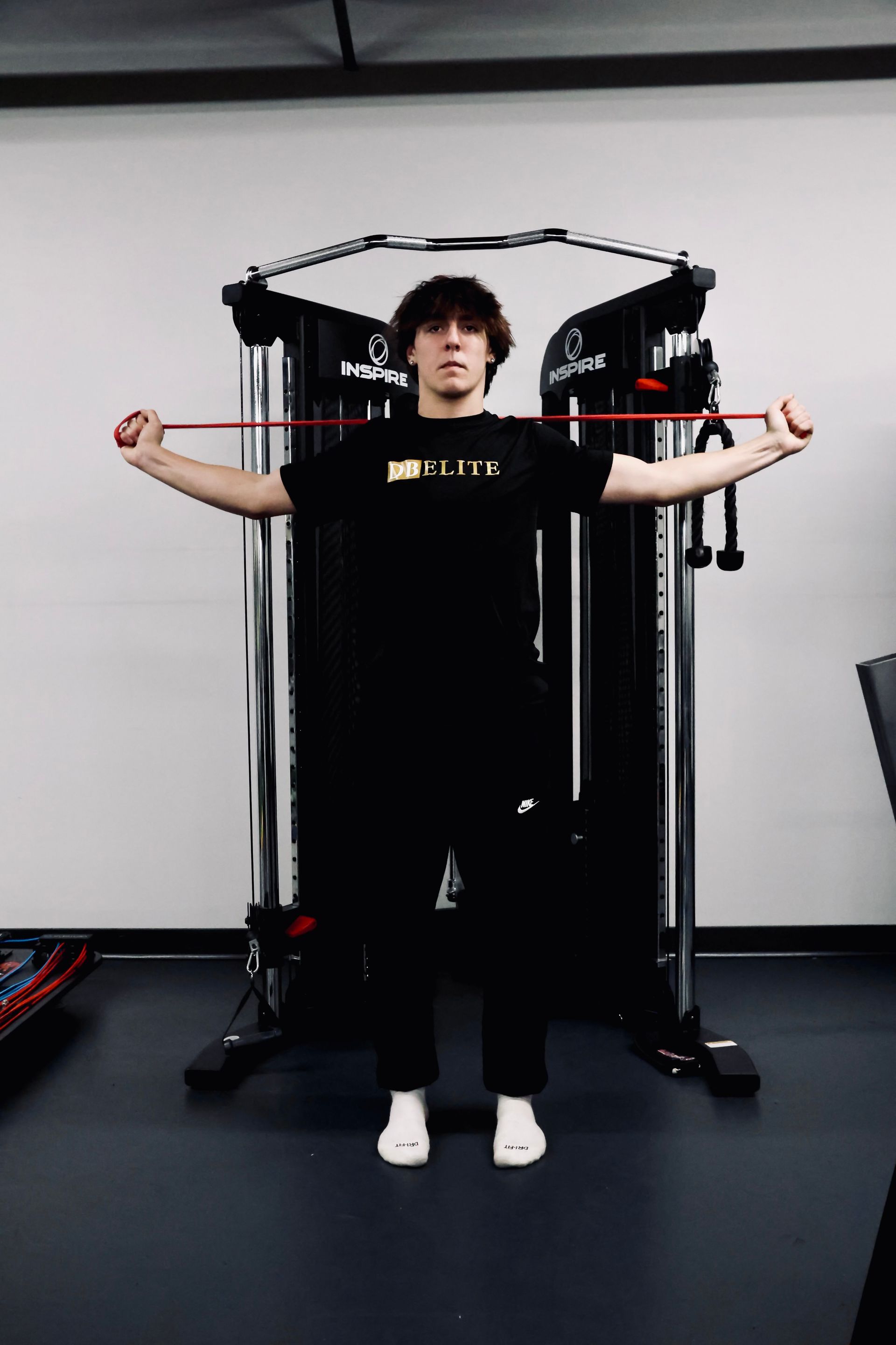 A man in a black shirt is holding a red resistance band over his shoulder.
