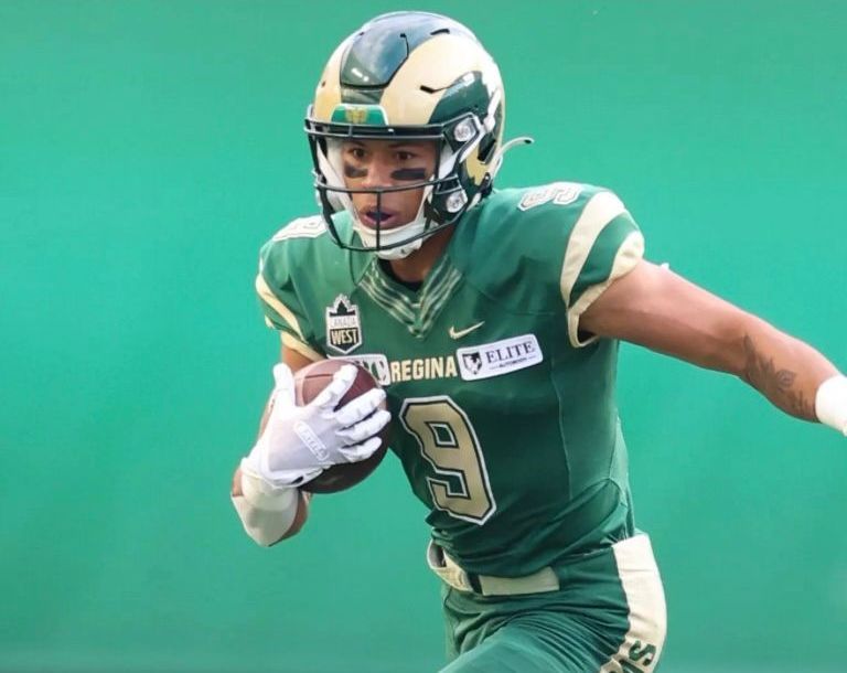 Football player in green uniform running with the ball.