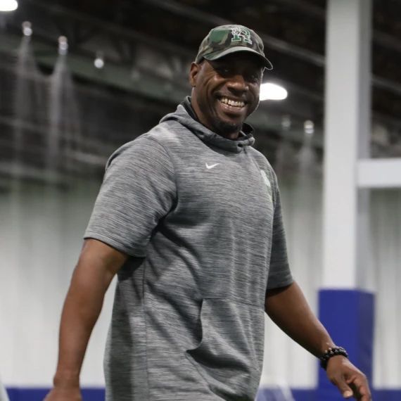 Smiling man in grey hoodie and camo cap, indoors.