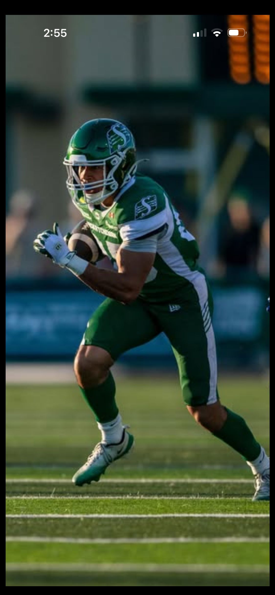 Football player in green uniform running on a field with the ball tucked in arms