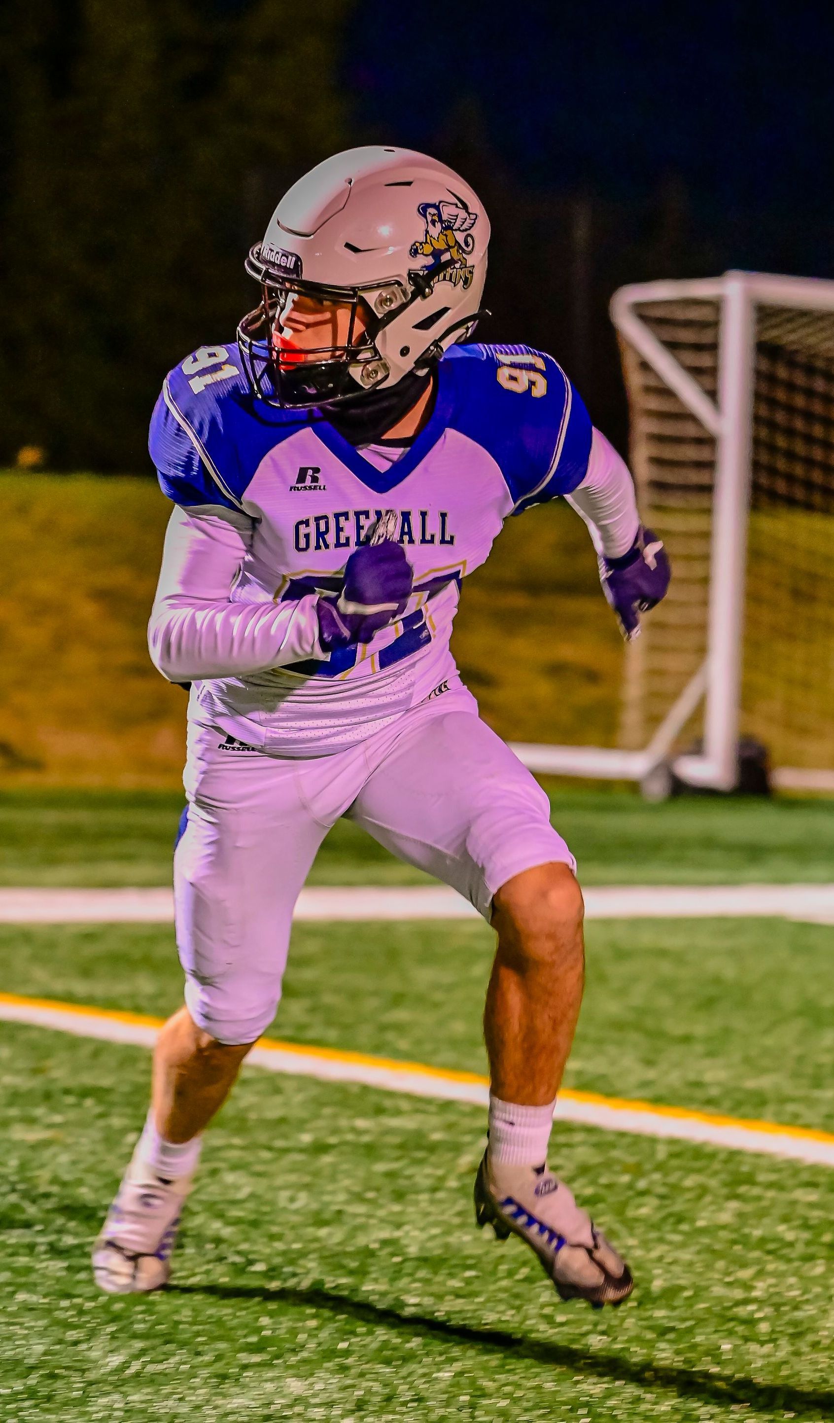Football player in white and purple uniform running on a green field.
