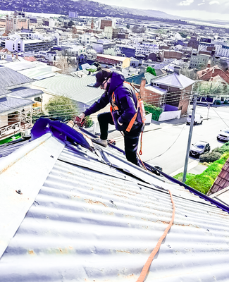 An employee working on top of a roof with a drill to replace a rusty metal roof with a new colourbond roof replacement with Launceston in the background