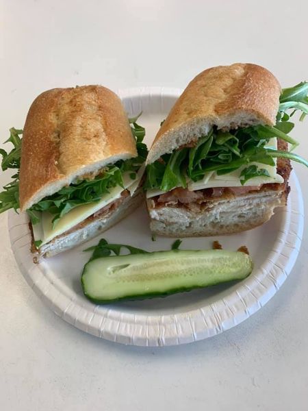 Sandwich on paper plate with pickle spear, filled with greens and sliced turkey or chicken