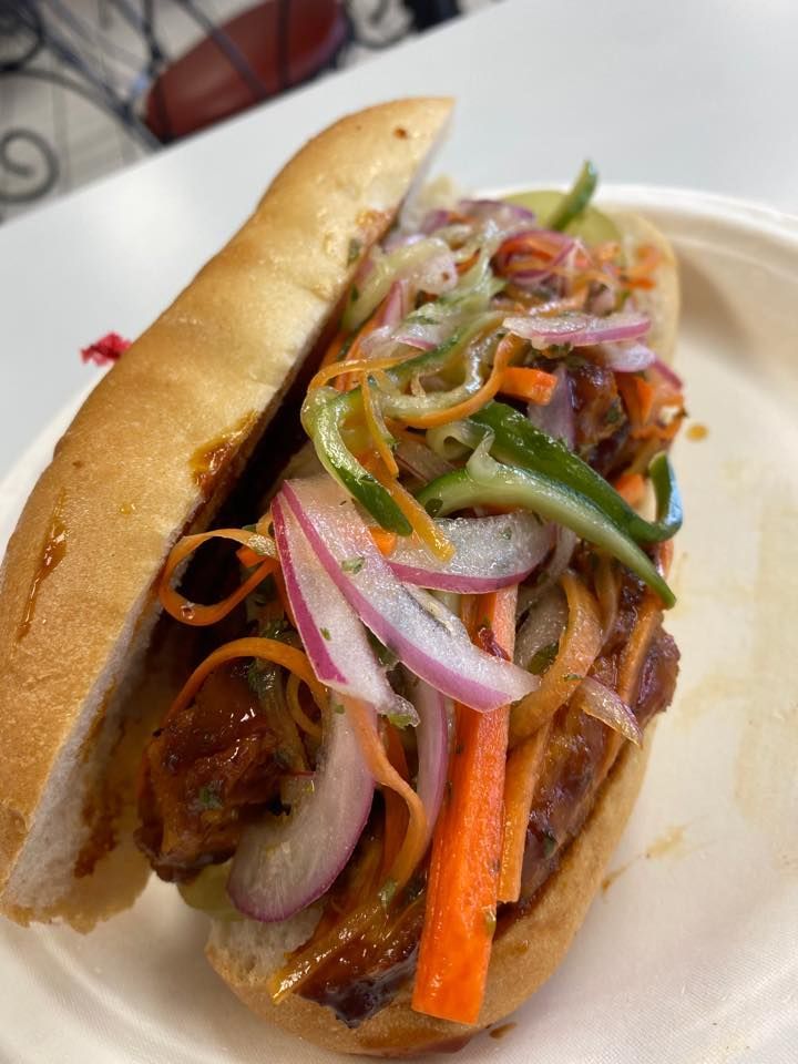 Sandwich topped with grilled meat and pickled vegetables on a white plate