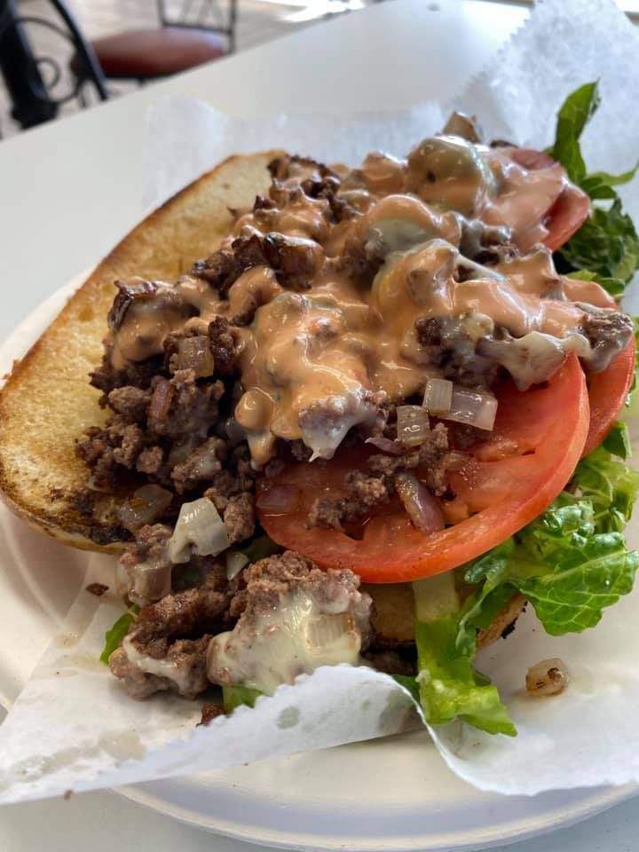 Sandwich with lettuce, tomato, ground meat, and creamy sauce on white paper wrappers