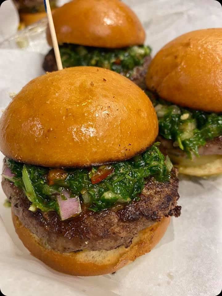 Three gourmet sliders with glossy buns topped with chopped green herbs and onions on a white tray