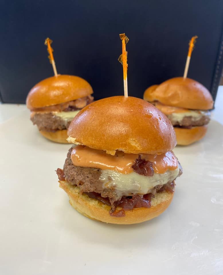 Three mini cheeseburgers with toothpicks on a white surface against a dark background