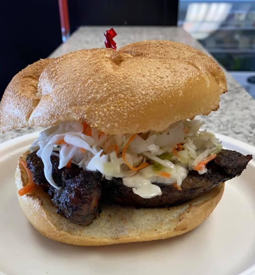 Close-up of a grilled sandwich with coleslaw on a white plate, topped with a sesame bun.