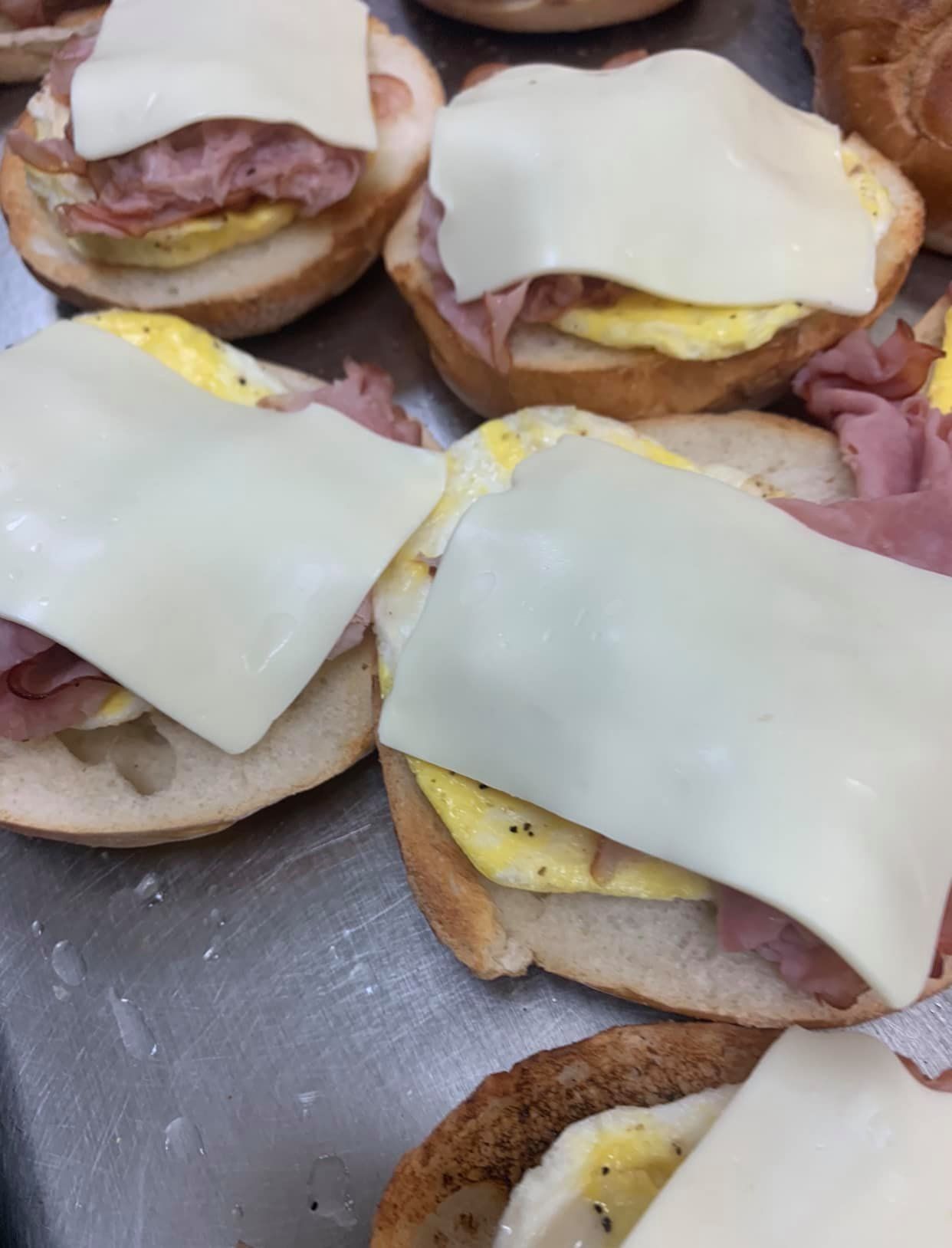 Open-faced breakfast sandwiches with eggs, ham, and melted white cheese on a metal tray.