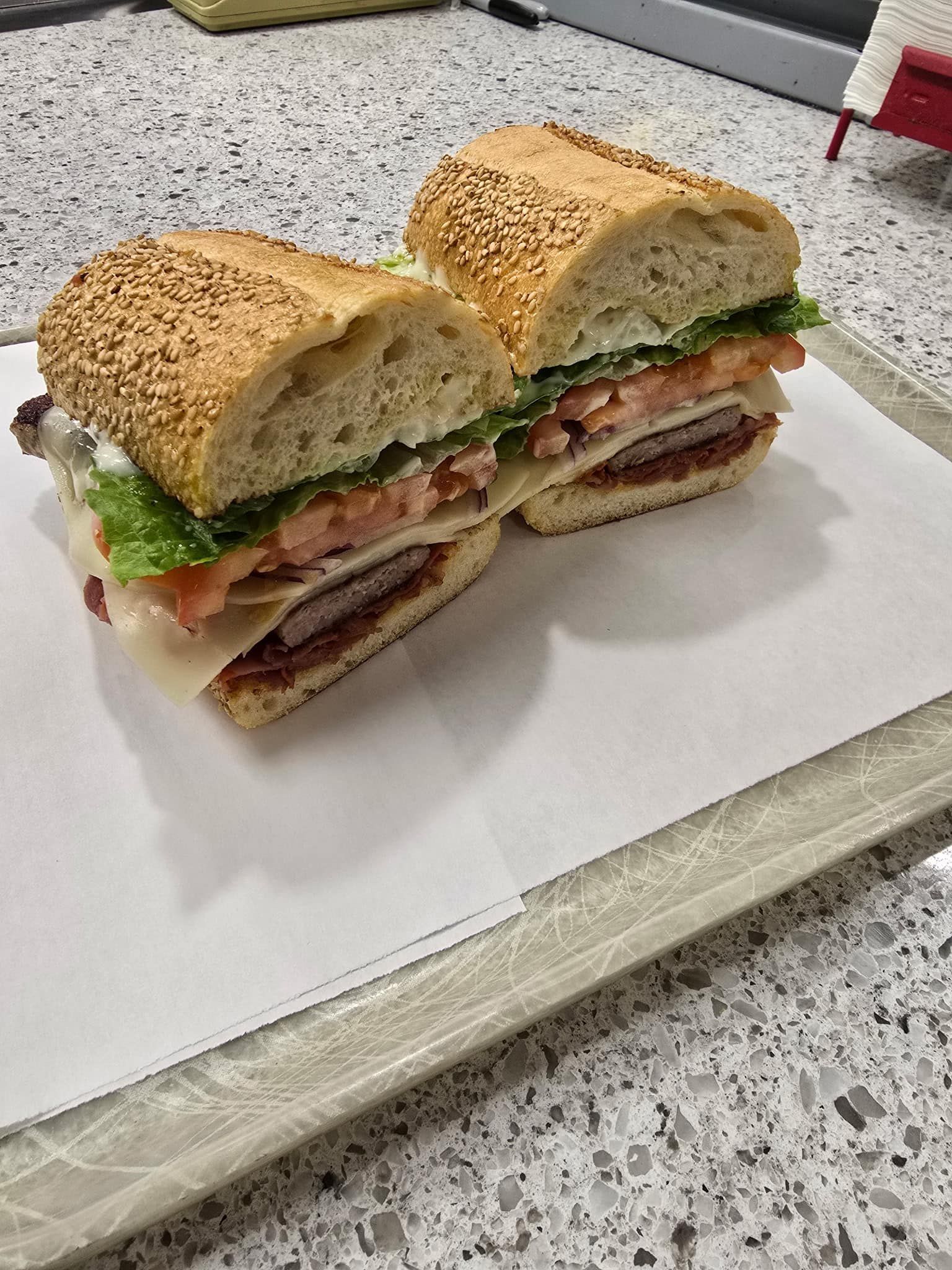 Cut sandwich with lettuce, tomatoes, and layered deli meat on a white tray in a kitchen.