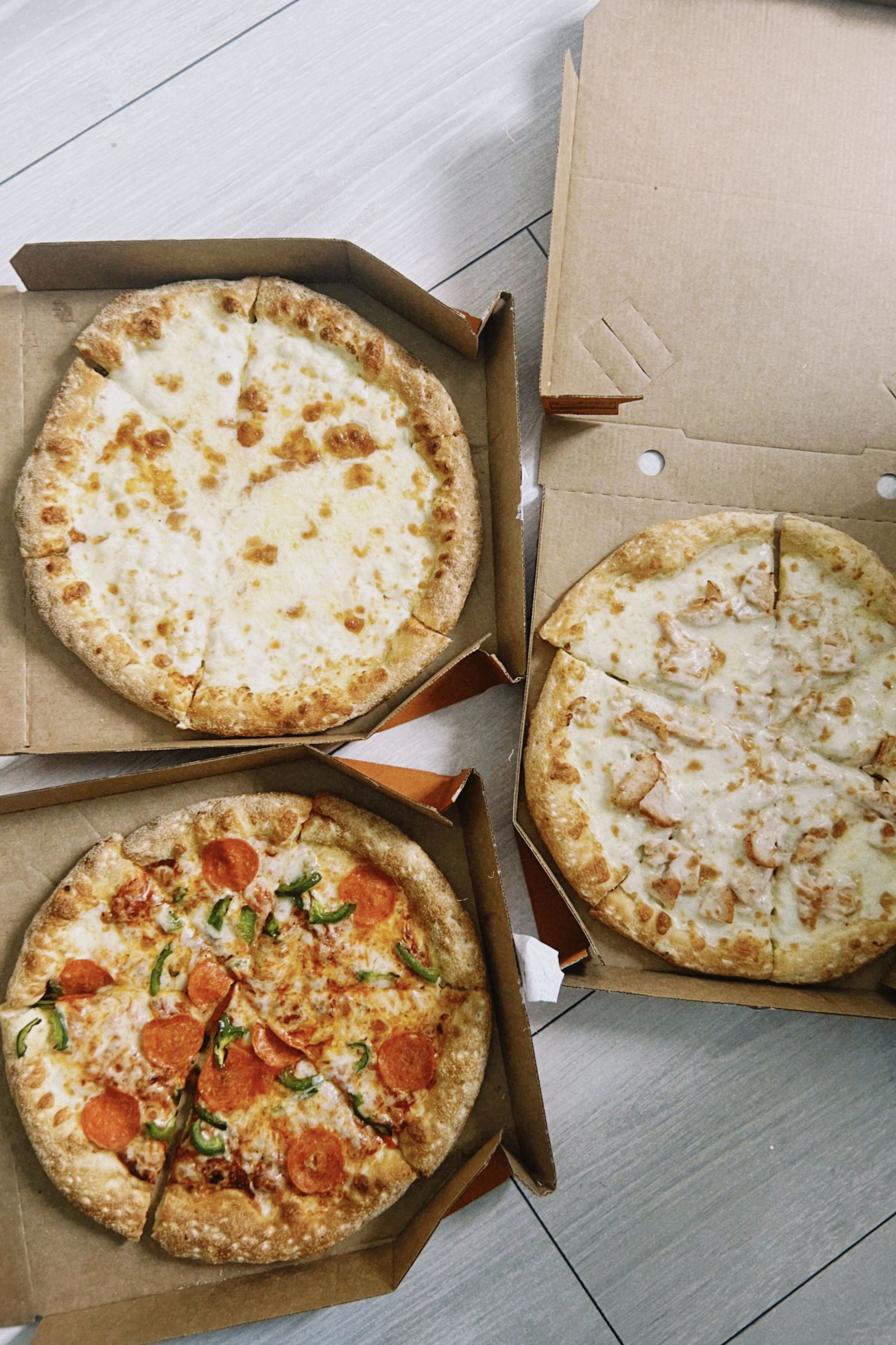 Three open pizza boxes on a floor, with two cheese pizzas and one topped pizza.
