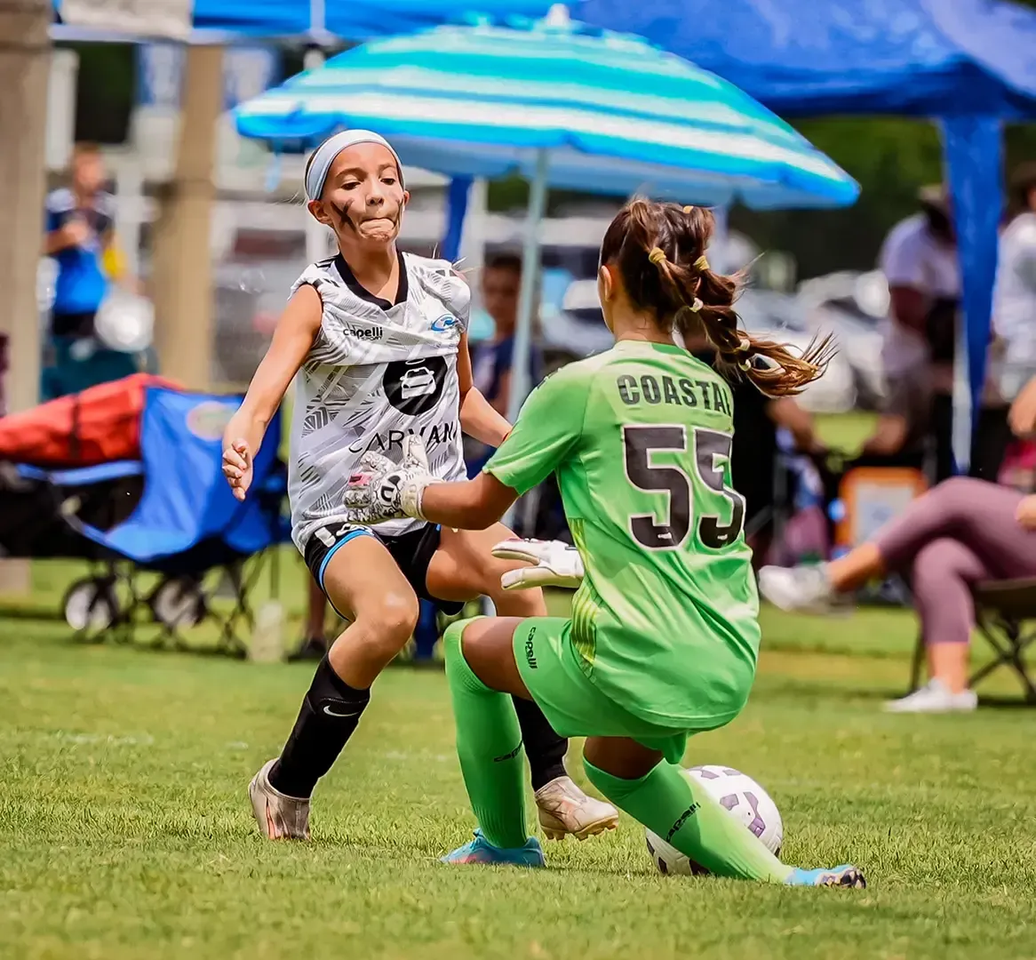 Soccer players in action: one advances towards the ball while the other attempts to block it on a green field.