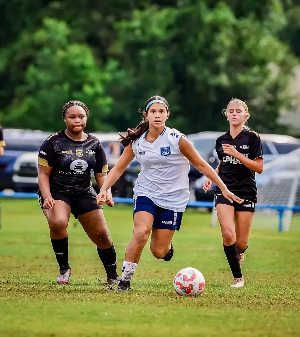 Soccer players on a green field. A player dribbles the ball between two opponents.