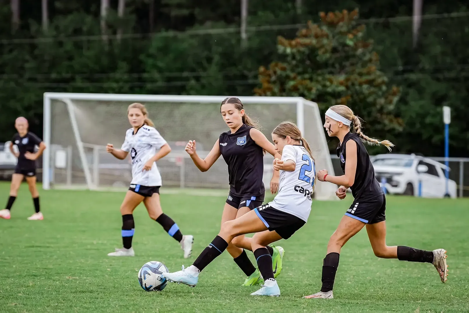 Soccer players in action on a green field. Two players in black uniforms compete for the ball.