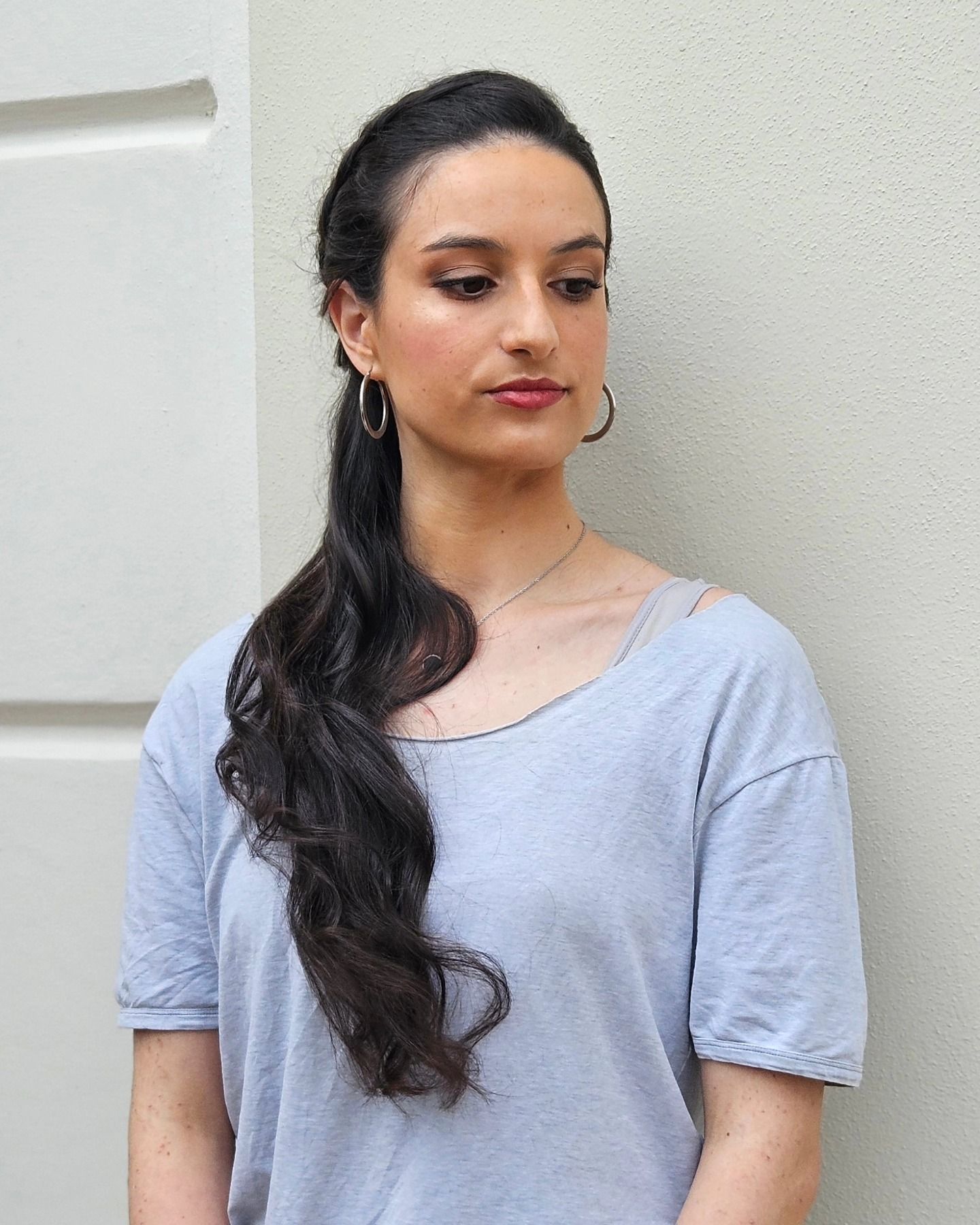Una donna con i capelli lunghi e gli orecchini a cerchio è in piedi davanti a un muro.
