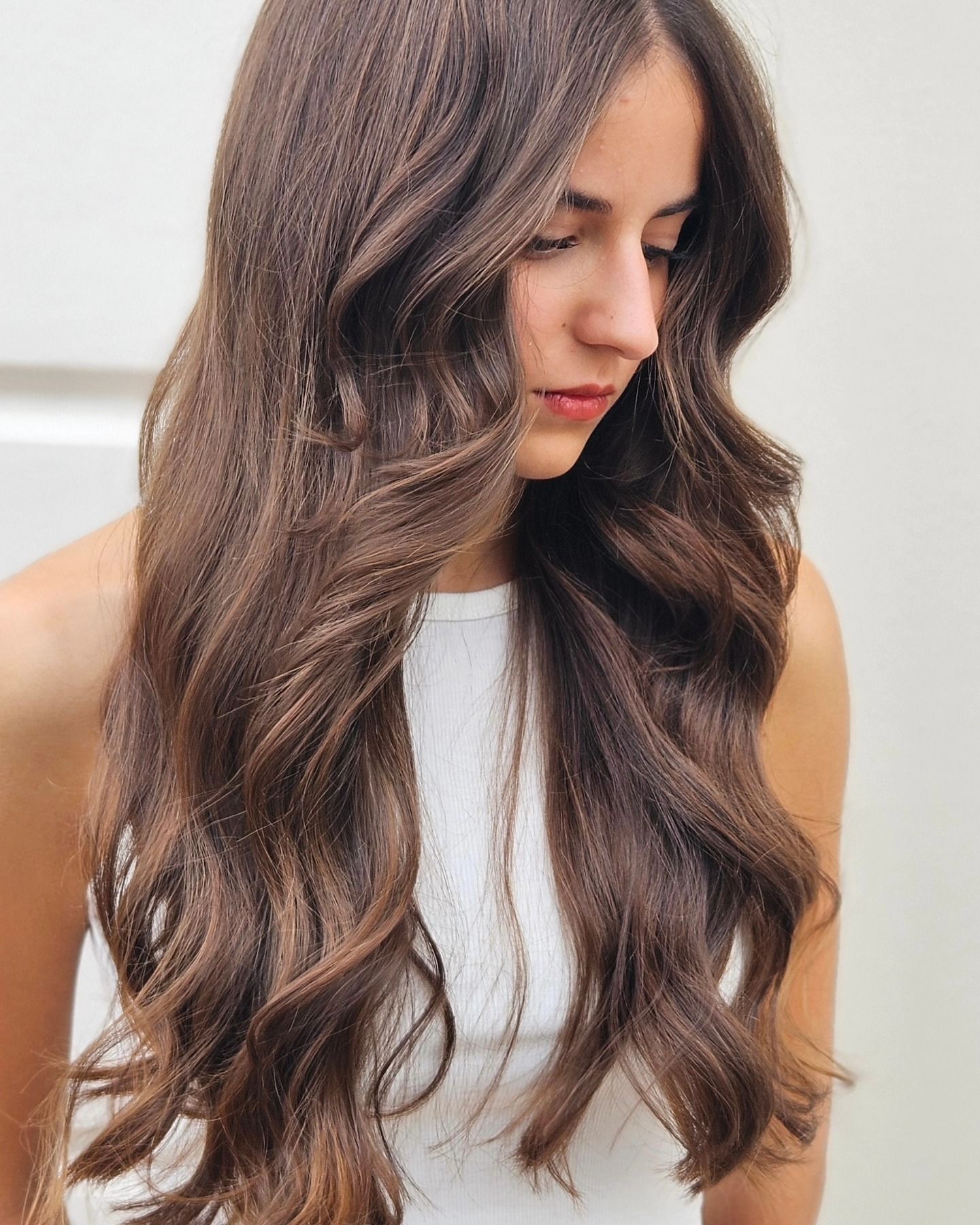 Una donna con lunghi capelli castani indossa una canottiera bianca.