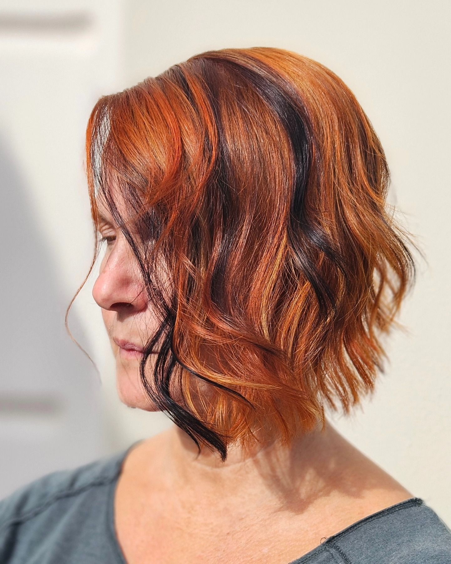 Una donna con i capelli rossi e mèches nere indossa una maglietta grigia.