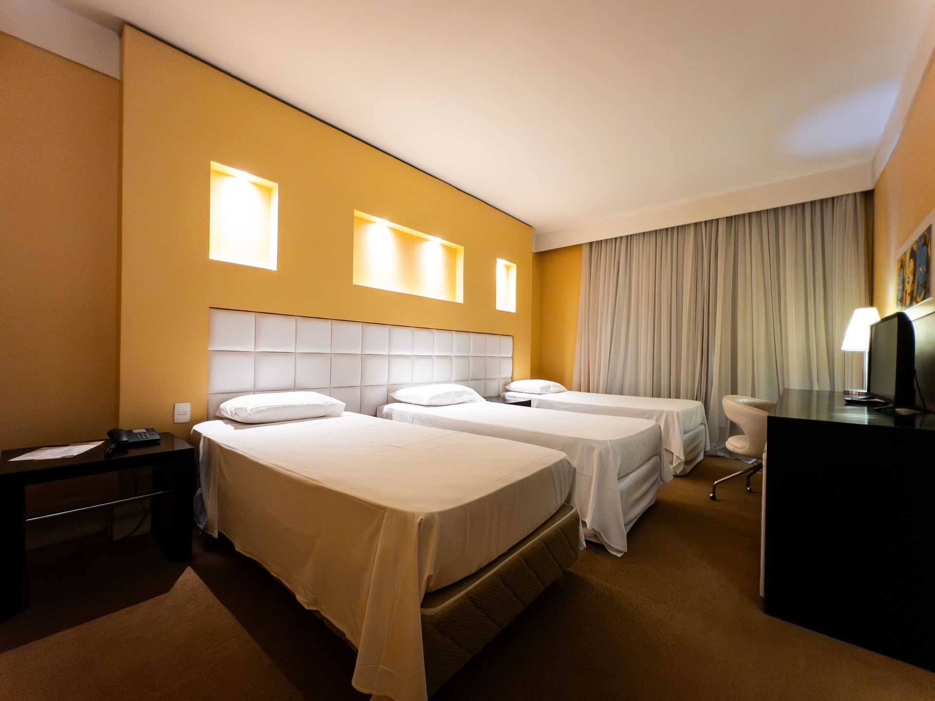 Um quarto de hotel com três camas, uma escrivaninha e paredes amarelas.