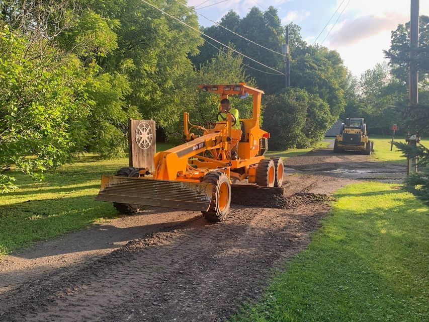 A man is driving a yellow tractor on a dirt road.