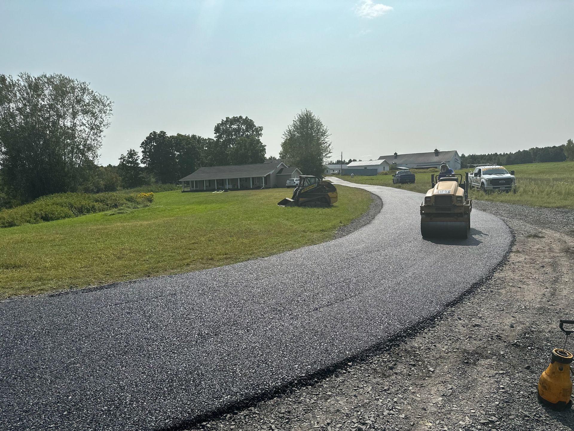 A road is being paved in a rural area with a house in the background
